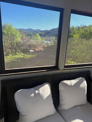 A window with a view of a mountainous landscape, a metal mesh screen, and a bench with cushions.