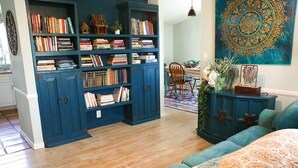 A cozy living room with a large blue bookshelf filled with books, a wooden coffee table with a vase of flowers, and a teal sofa.