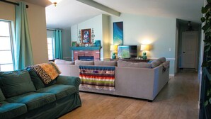 A living room with a green sofa, a gray sofa, and a TV. There is a fireplace with a mantel and a painting above it.