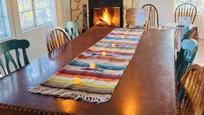 A dining room with a long wooden table, stone fireplace, and chairs.