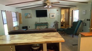 A room with a wooden dining table, a ceiling fan, a television, and a green armchair.