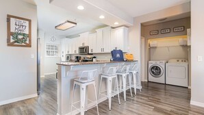 Una cocina moderna con armarios blancos, una isla central con taburetes y un microondas, además de una lavadora.