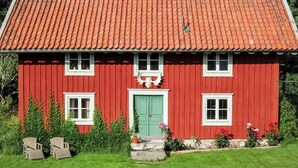 Une maison en bois rouge avec une porte verte, des fenêtres blanches et un toit recouvert de tuiles.