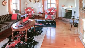 Un salon chaleureux avec un canapé à rayures, des fauteuils à motifs floraux, une table basse en bois et une cheminée.