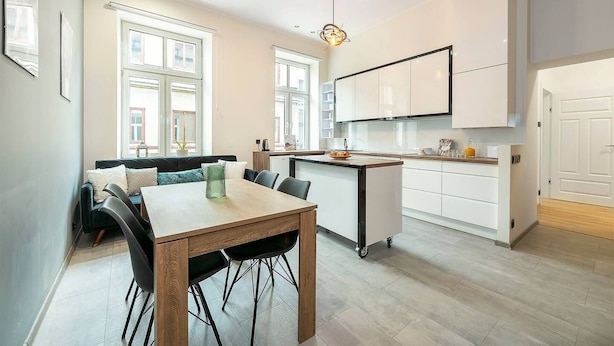 Una cocina moderna con armarios blancos, una zona de comedor con mesa y sillas de madera, y una isla de cocina con un frutero.