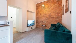 Un salón moderno con pared de ladrillo, un televisor de pantalla plana, un sofá color turquesa y una pequeña mesita auxiliar.