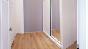 Un pasillo estrecho con suelo de madera, una puerta blanca y una puerta corredera de vidrio que da a una habitación.
