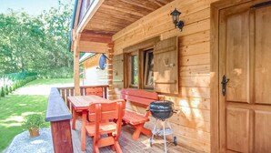Een houten chalet met een overdekte veranda, een barbecue en een eettafel met stoelen.