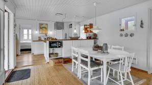 Een moderne keuken met witte kasten, een eetgedeelte met witte stoelen, en een houten vloer.