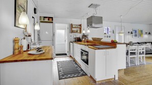 Een compacte keuken met witte kasten, een houten aanrechtblad en een inbouwoven. Er is een klein zite hoekje met een witte tafel en stoelen.