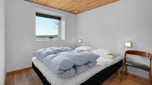 Ein Schlafzimmer mit Bett, Fenster, Stuhl und einer Wandleuchte.