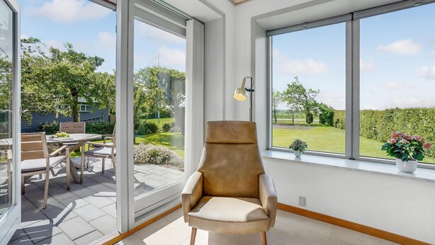 Ein modernes Zimmer mit großen Fenstern, einem bequemen Sessel und einer Essecke mit Außenbereich.