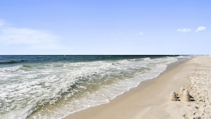 Ein Strand mit Wellen, blauem Himmel und einigen Sandskulpturen.
