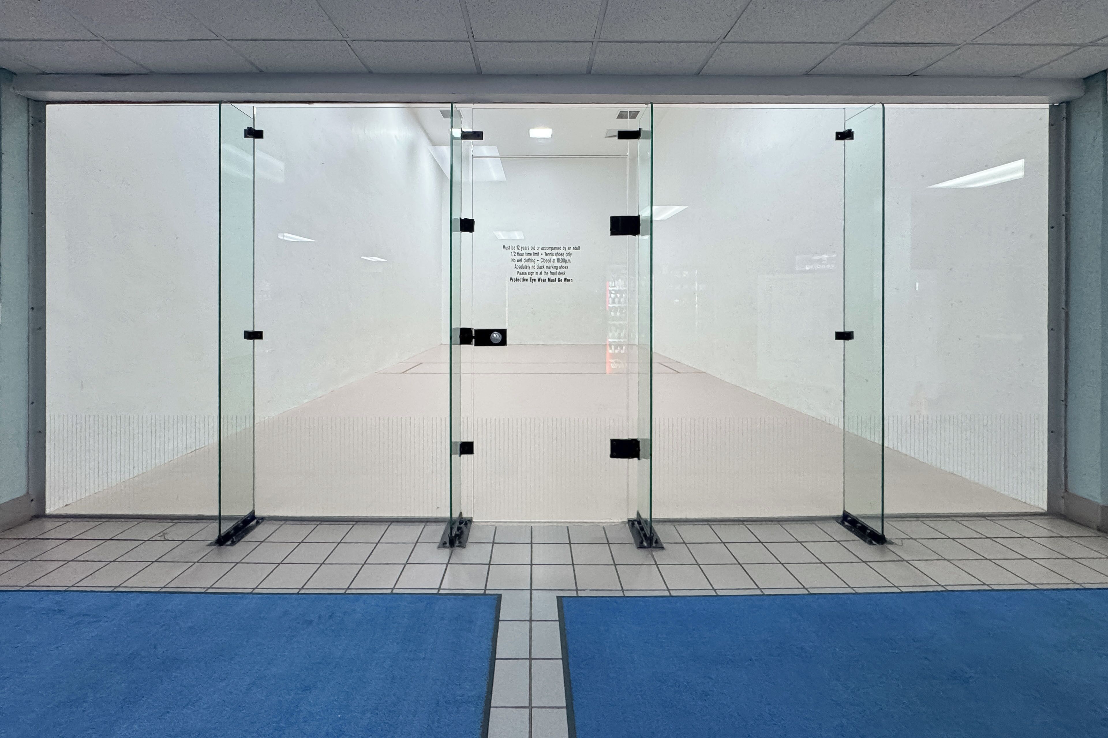 A room with a glass partition, a blue carpet, and a sign on the glass.