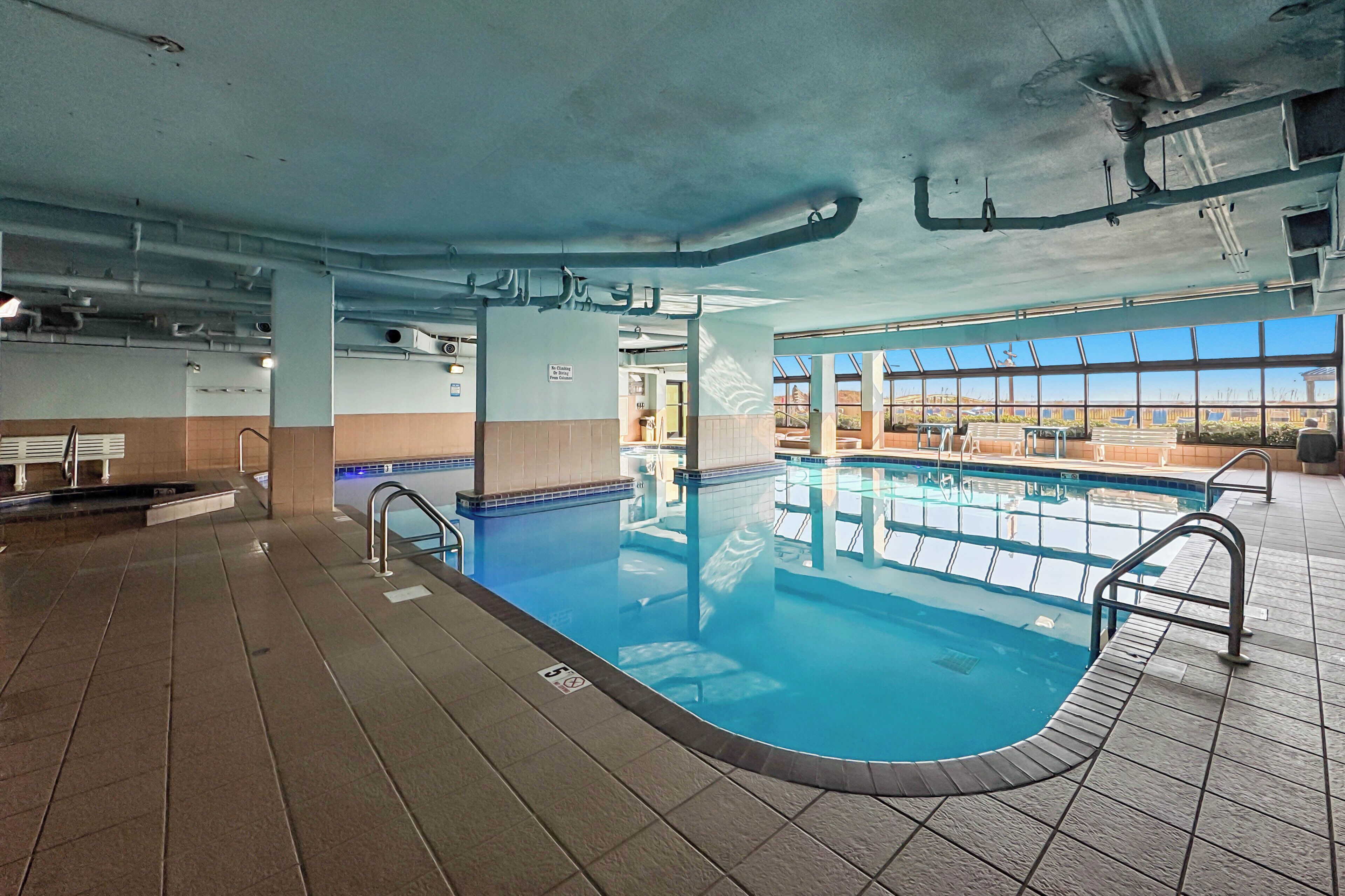 Una piscina interior con suelos y paredes de azulejos, barreras de cristal transparente y vistas al exterior a través de amplias ventanas.