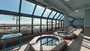 Ein Poolbereich auf dem Dach mit mehreren Whirlpools und einem Tisch, große Fenster bieten Blick auf die Stadt.