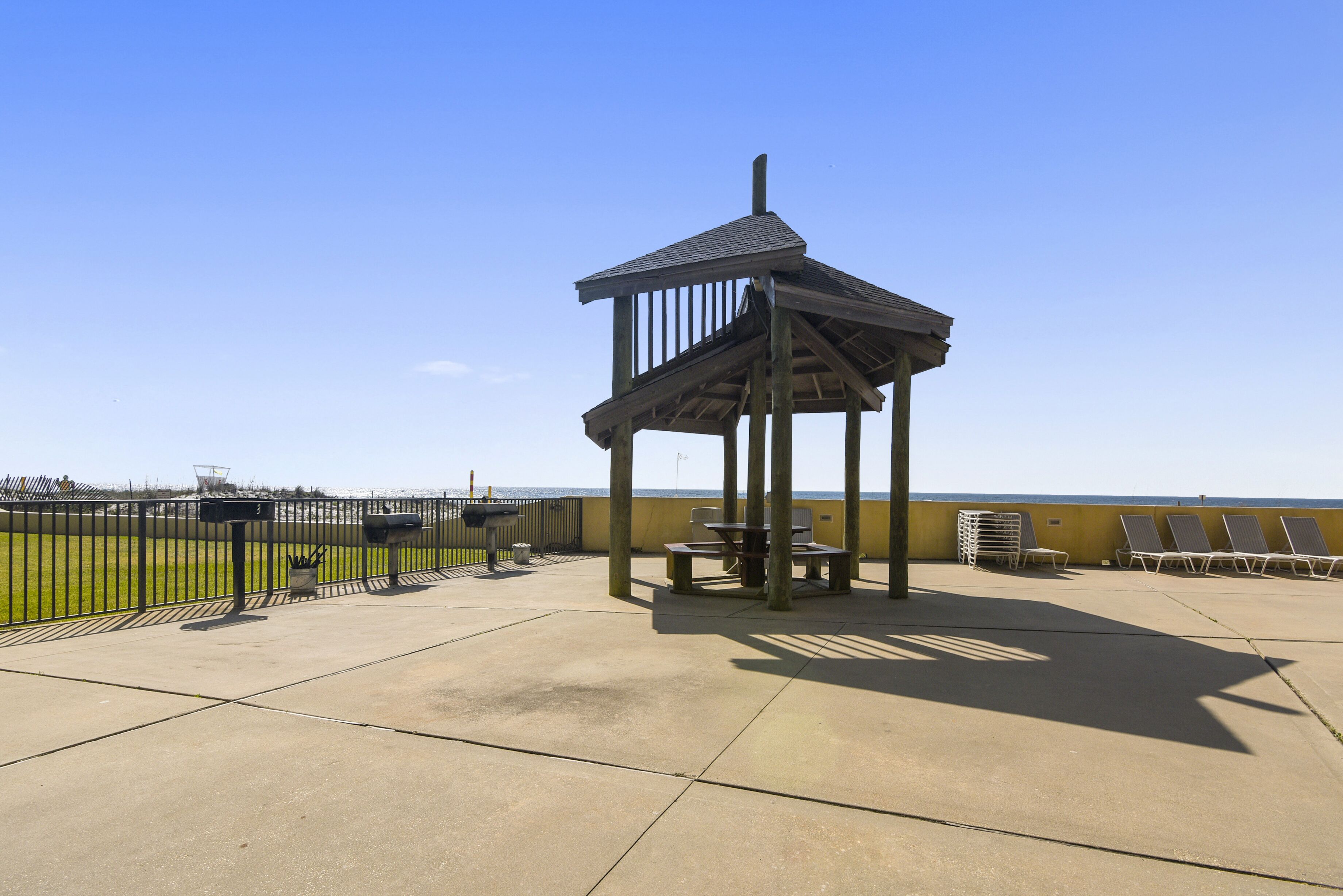 Un área de estar al aire libre con techo, un gazebo de madera, suelo de hormigón y vista a la playa.