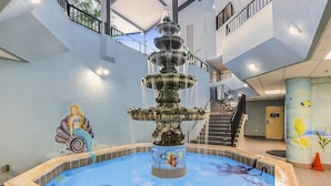 Ein mehrgeschossiges Atrium mit einer zentralen Fontäne, einem Wandgemälde einer Meerjungfrau und einer Treppe.