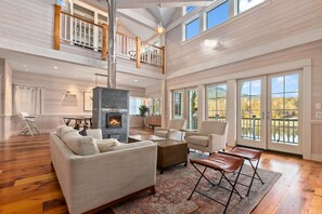 A spacious living room with a fireplace, high ceilings, and large windows offering a view of the outdoors. - Beautiful Home on Lake Samish with Deck- 10 minute drive to Fairhaven (Bellingham)