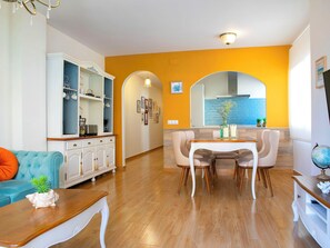 A modern living room with a dining area, a kitchen with a blue backsplash, and a large mirror.