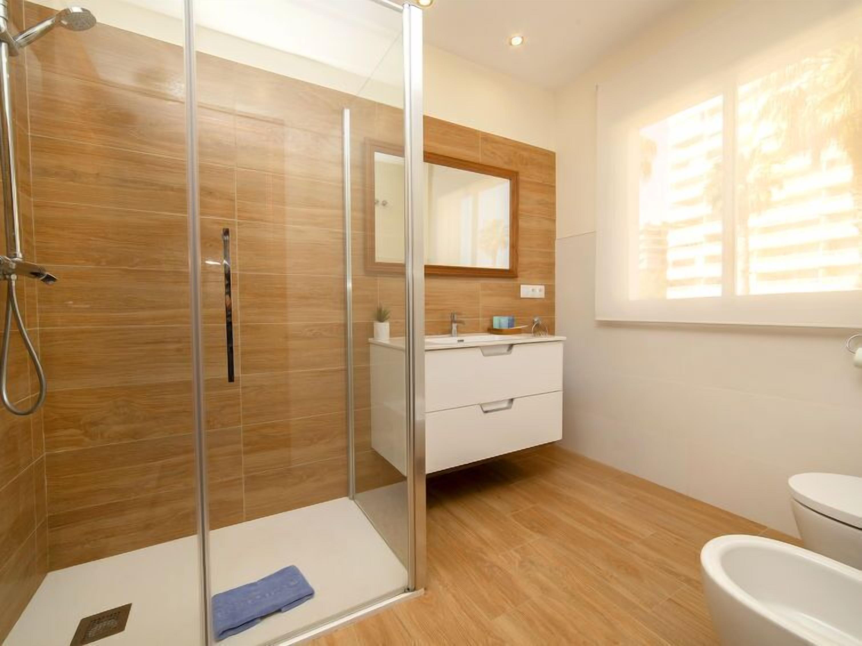 A modern bathroom with a glass-enclosed shower, a white vanity with a mirror, and a toilet.