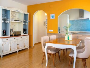 A dining area with a wooden table and chairs, a white cabinet with kitchen appliances, and a blue brick backsplash.