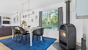 A modern living room with a dining area, a fireplace, and large windows overlooking a forest.