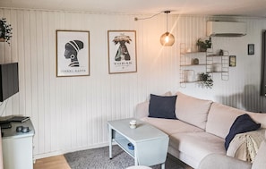 Een woonkamer met een bank, een bijzettafeltje, een televisie en twee ingelijste foto’s aan de muur.