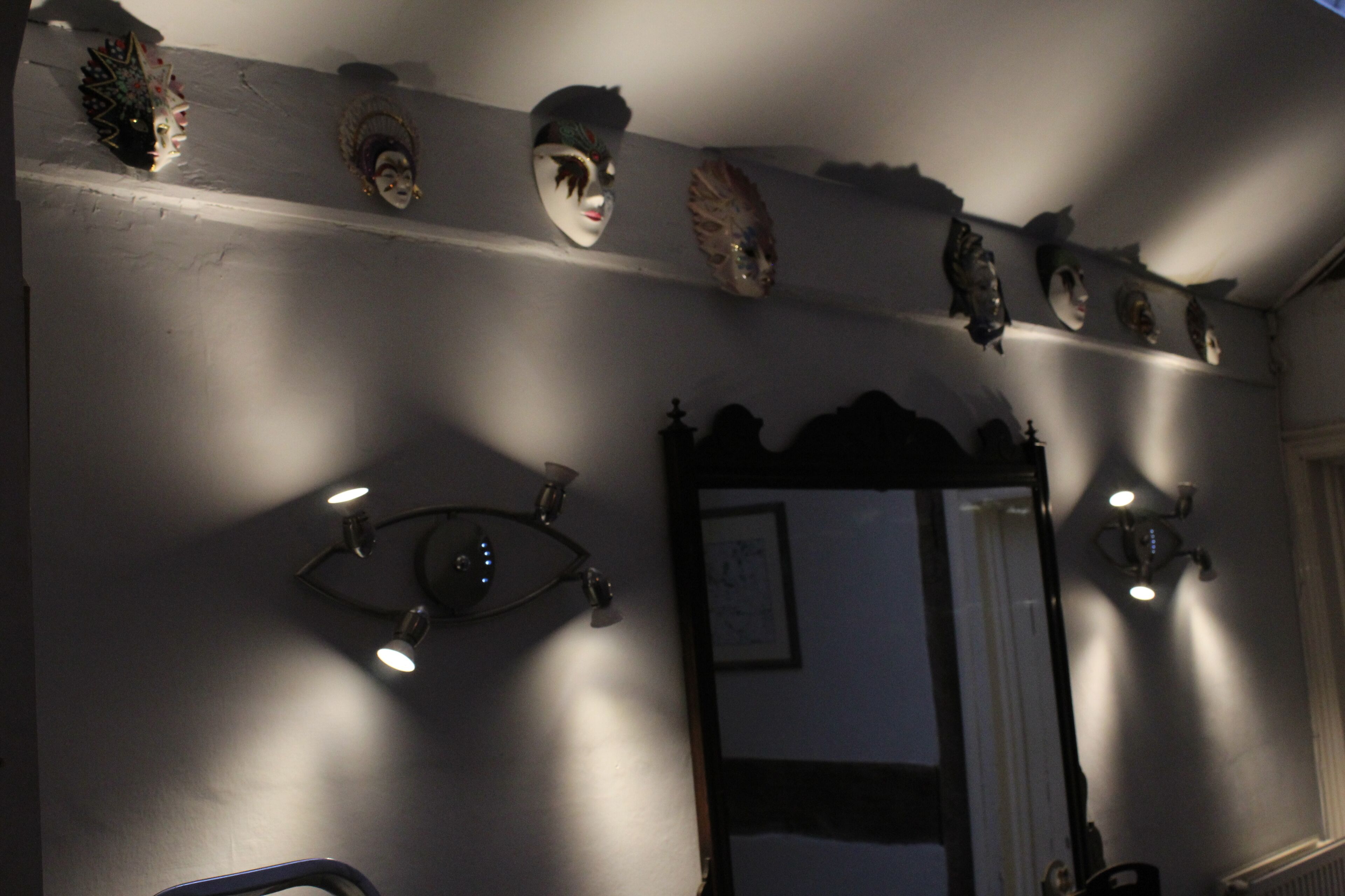 A bathroom with multiple mirrors, wall-mounted lights, and decorative masks.