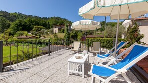 Una terraza con mobiliario exterior, sombrillas y vistas a una colina.