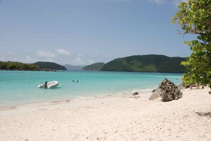 Een strand met helder turquoise water, wit zand en rotsformaties.