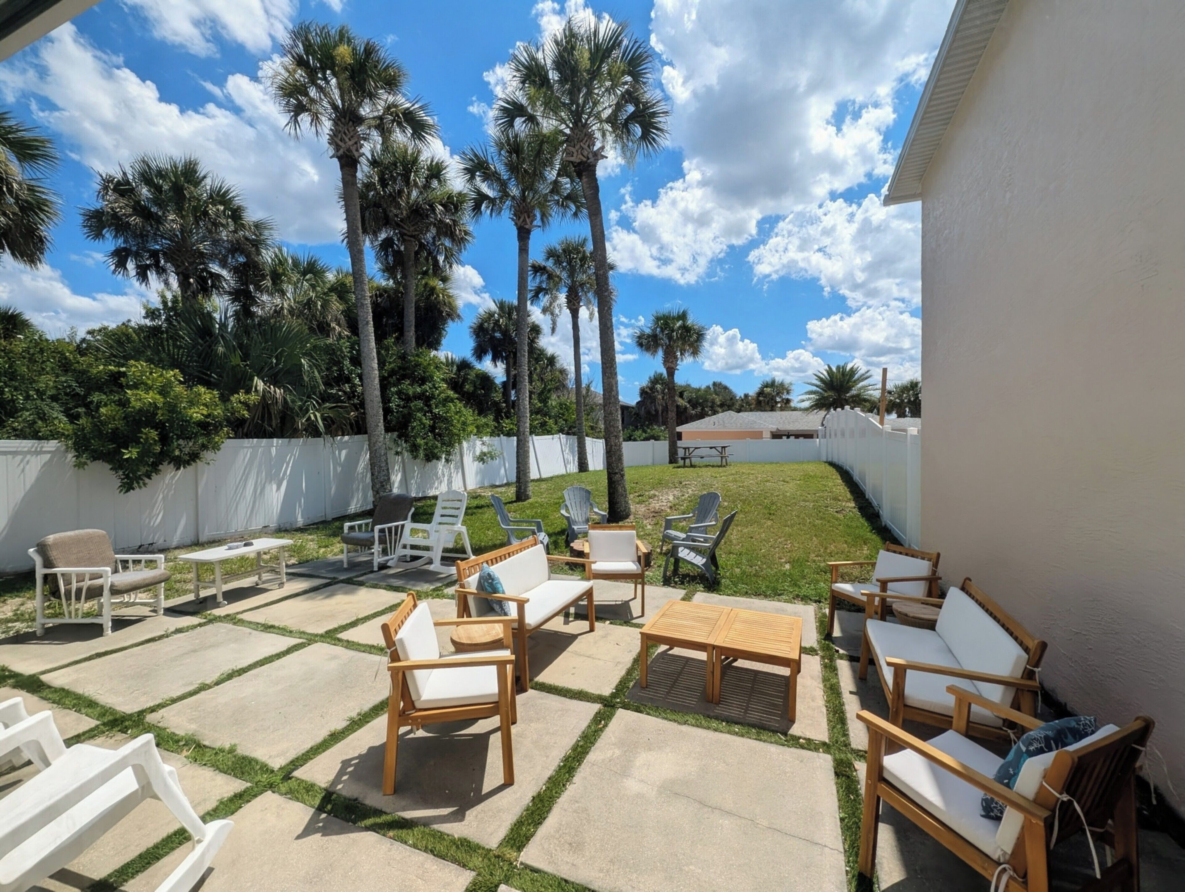 An outdoor patio with wooden furniture, a white fence, and palm trees.