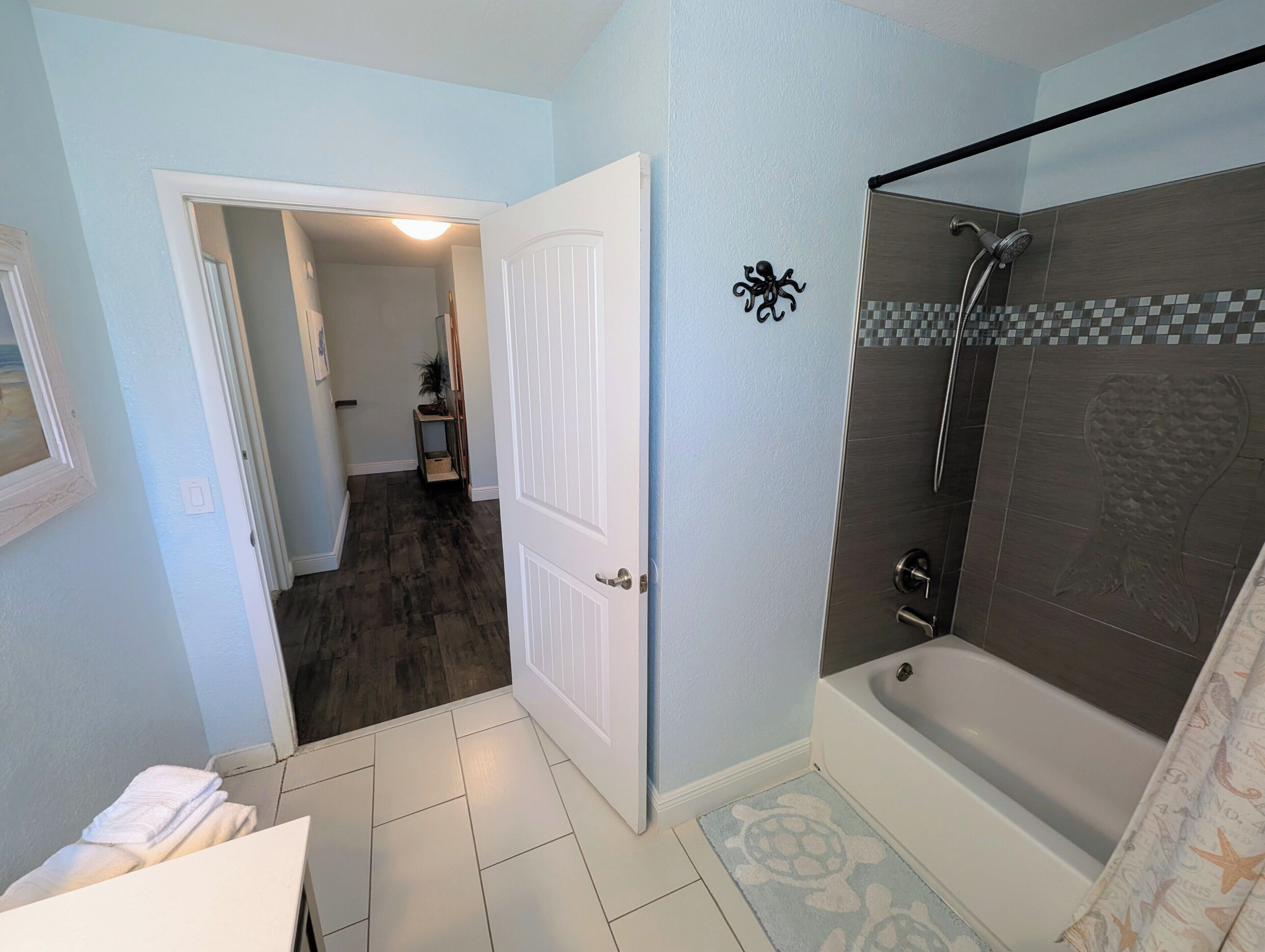 A bathroom with a shower, a door leading to another room, and a tiled floor.