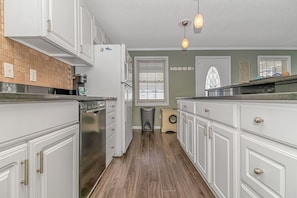 A kitchen with white cabinets, a dishwasher, a washing machine, and a window with blinds.