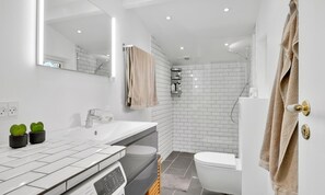 A modern bathroom with a white sink, mirror, and white-tiled shower area.