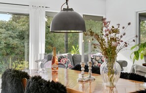 Ett matbord med en flaska champagne, glas och ljus. Det finns ett stort fönster med utsikt över grönområden utanför.