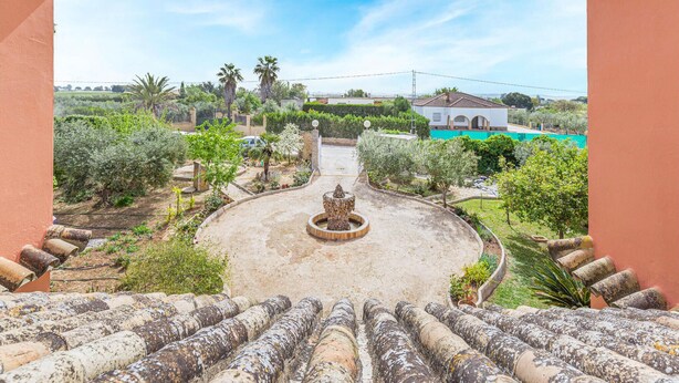 A courtyard with a fountain, surrounded by greenery and a view of a white building.