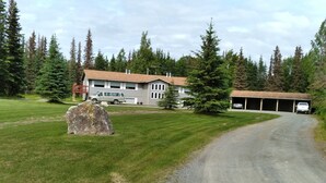 Une allée de gravier mène à une maison avec un garage, qui est entourée d’une pelouse et d’arbres.