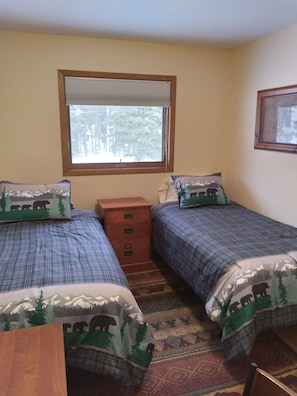 A bedroom with two beds, a wooden nightstand, a window with a view of trees, and a patterned rug.