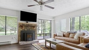 A living room with a fireplace, a sofa, a television, and large windows.