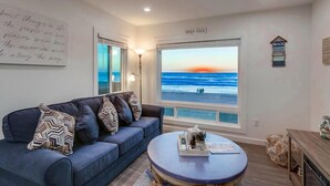 A living room with a large window overlooking the beach, a blue sofa with patterned cushions, and a coffee table with decorative items. - Ocean Front * Top Level + Sky Deck * Dog OK (San Diego)