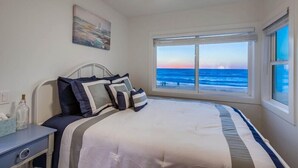 A bedroom with a bed, a nightstand, a window with a view of the ocean, and a painting on the wall. - Ocean Front * Top Level + Sky Deck * Dog OK (San Diego)