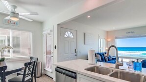 A modern kitchen with a view of the ocean, a dining area with a table and chairs, and a blue sofa by the window. - Ocean Front * Top Level + Sky Deck * Dog OK (San Diego)