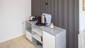 Una kitchenette con cafetera, tostadora y un tarro de crema en la encimera.