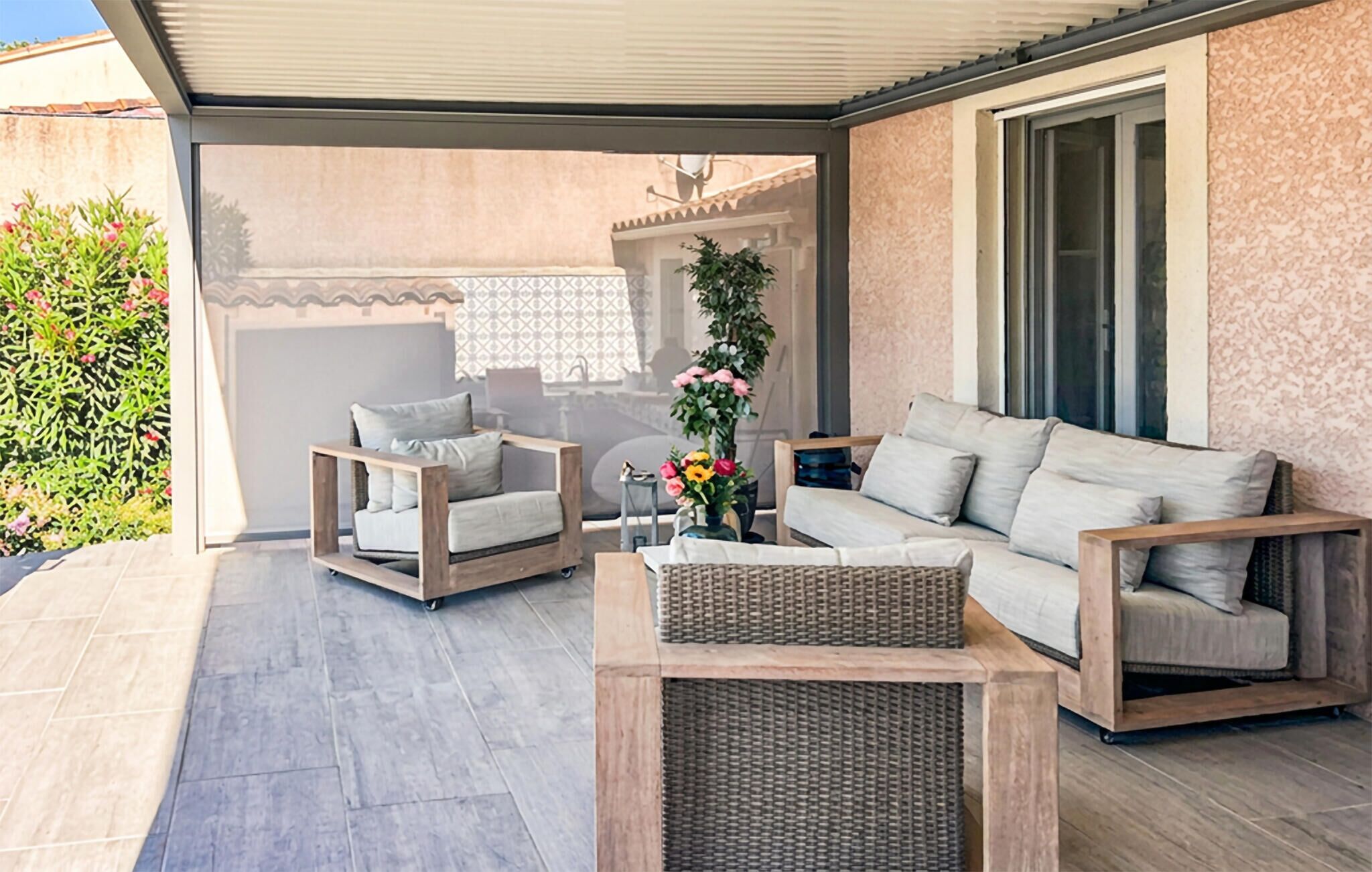 Een overdekt terras met twee banken en twee stoelen, een bijzettafeltje en een decoratieve plant.
