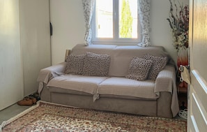 A cozy room with a beige sofa, patterned rug, and a window with curtains.
