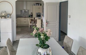 A dining area with a table set for four, a vase with flowers, and a kitchen in the background.