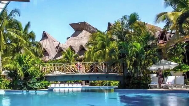 Un área de piscina con un puente, palmeras y montañas al fondo.