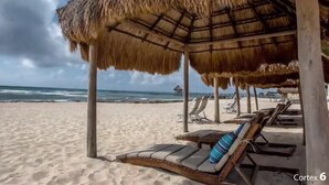 Una playa con sombrillas de paja y sillones de madera.