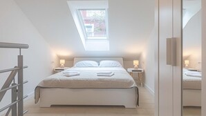 A modern bedroom with a skylight, a bed with white linens, two bedside tables with lamps, and a wooden floor. - 2 bedroom beach front home in Okrug Gornji (Okrug Gornji)